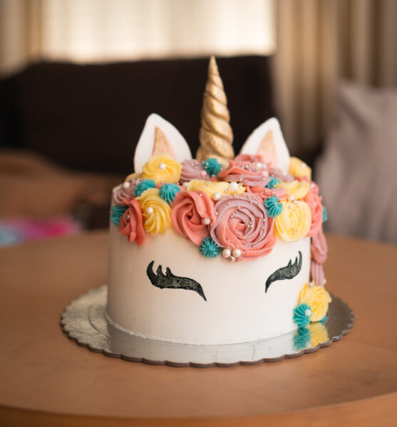 A whimsical unicorn-themed cake adorned with colorful frosting roses and a golden horn takes center stage on a birthday celebration table. High quality photo